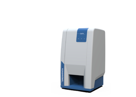 A Hydra full station, featuring a high-performance PC along with a monitor and printer, stands on a pristine white surface; it is a white and blue rectangular electronic device that resembles a printer with a front slot.