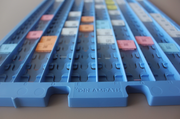 Close-up of a blue sorting tray, in the style of Crystal Trays (20/Pack), featuring labeled slots with various colored paper labels.