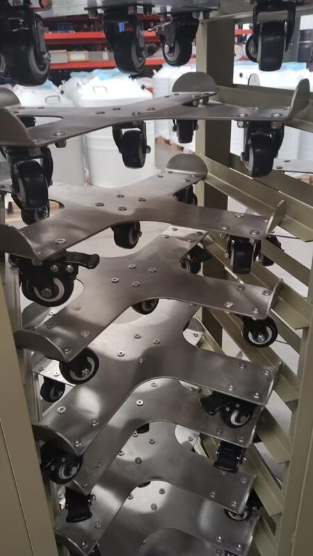 A rack in an industrial setting holds a stack of Mobile Trolleys suitable for 65-175lt series products, each equipped with 5 casters.