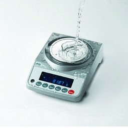 Digital weighing scale with water being poured onto its surface, displaying a reading on its screen.
