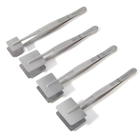 Four metal paddle forceps with flat paddle ends are arranged diagonally on a white background.