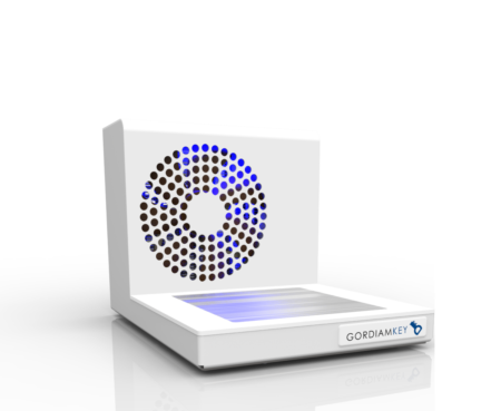 A low-profile and lightweight white electronic device branded “GORDIAMKEY” on the front, the Cryoplate 4X Mini for 12 cassettes features a perforated circular panel with blue LED lighting and a flat touchpad area, seamlessly combining modern aesthetics with practical functionality.